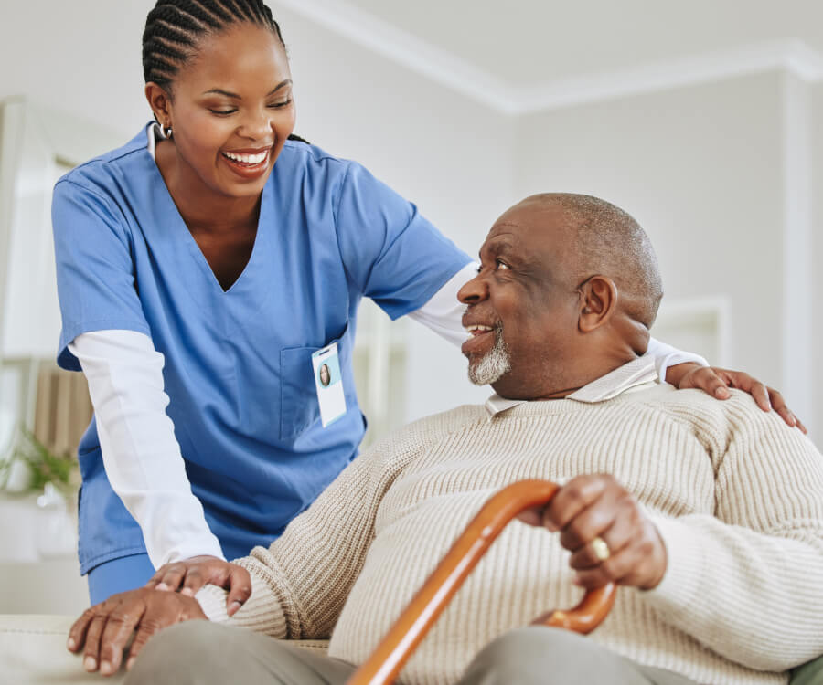 happy nurse with her hand on the shoulder of an older patient with a cane