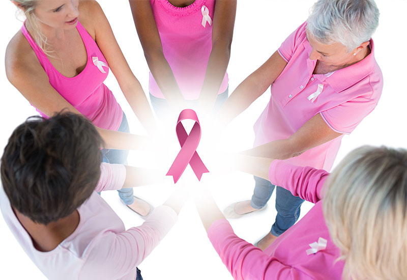 five women wearing pink with their hands in the middle with breast-cancer ribbon