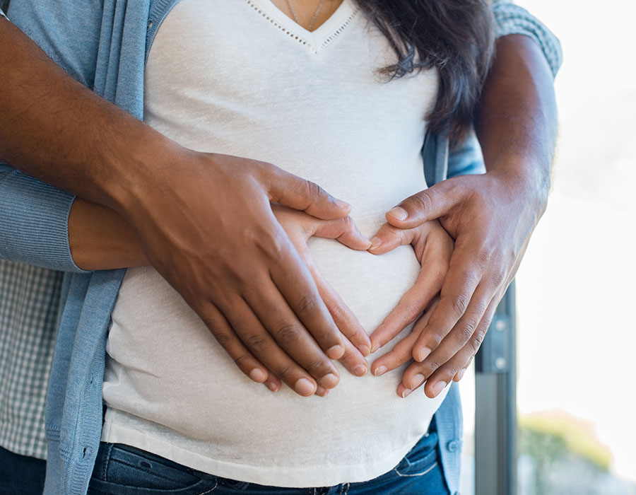 pregnant woman and husband holding pregnant belly in the shape of a heart