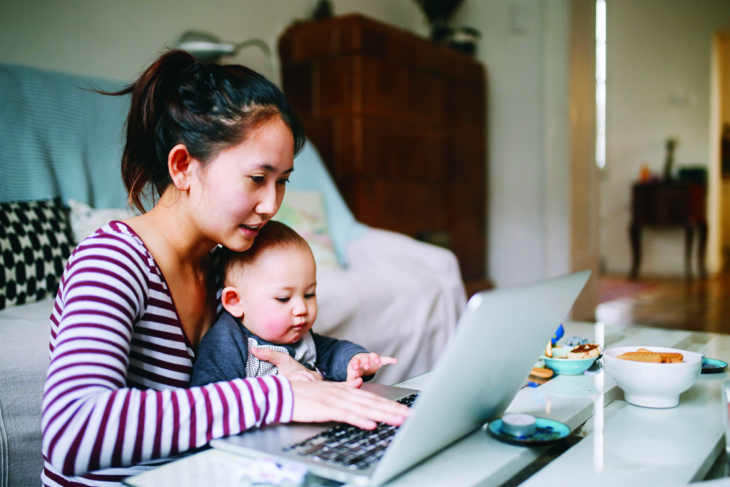 Asian mother on her computer with her baby on her lap.