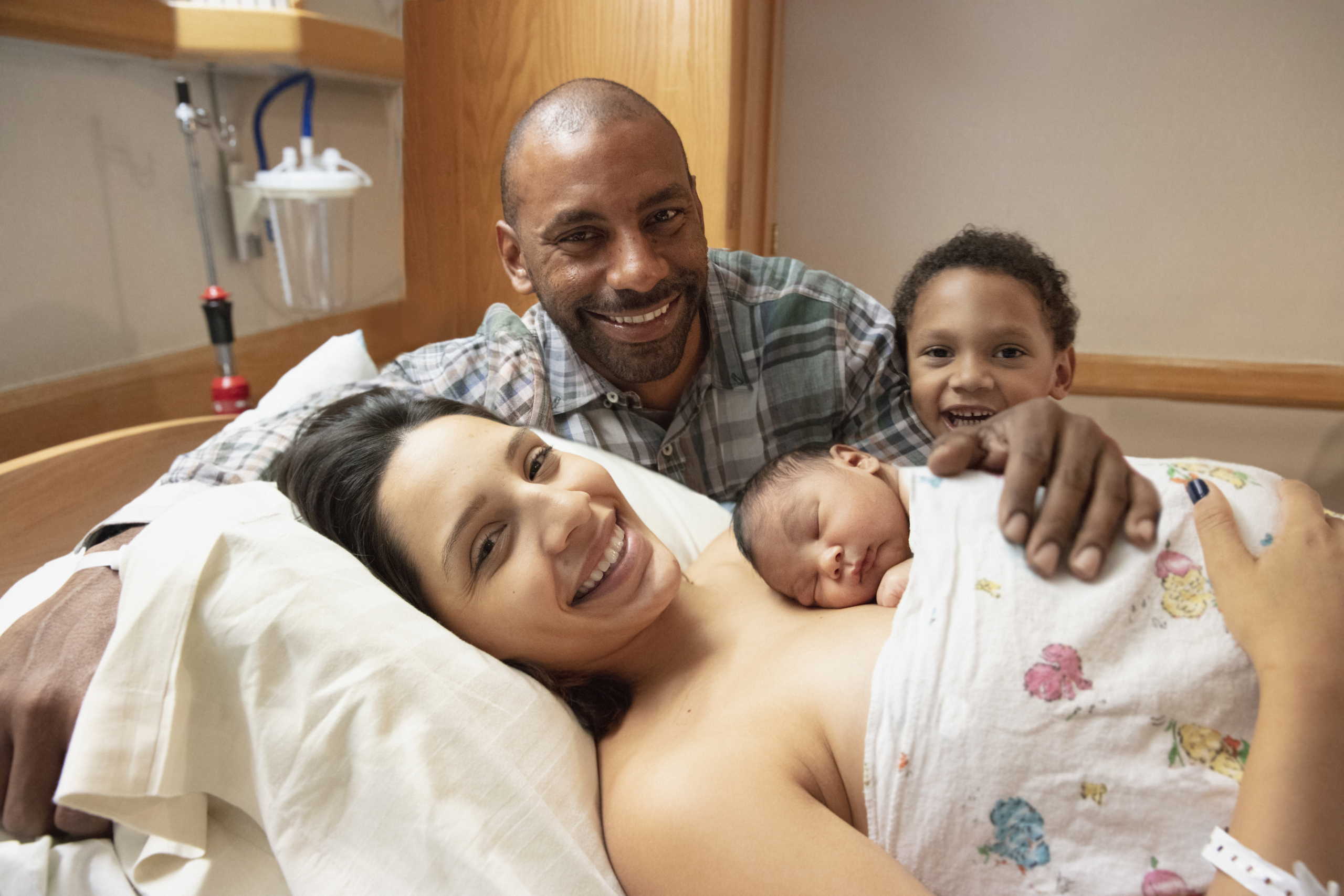 mother holding newborn in hospital bed as father and older son look on